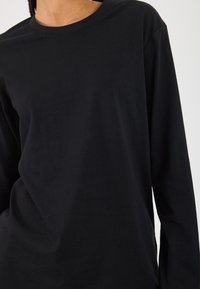 Schwarz langärmliges T-Shirt aus weichem Baumwollstoff, mit rundem Ausschnitt und minimalistischem Design ohne sichtbare Muster oder Akzente.