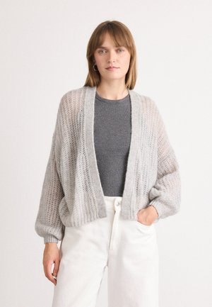 Lichtgrijze gebreide cardigan met een open voorkant, een losse pasvorm en geribbelde boorden, gedragen over een grijze top en witte broek, met een textuurpatroon.
