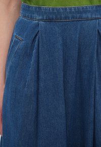 Gonna di denim di un blu scuro, con pieghe, tasche laterali e una superficie liscia. Vita alta con dettagli di cuciture a contrasto.