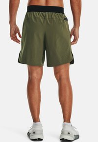 Gröna sportshorts med ett svart midjeband, med perforerade designelement på sidorna för andningsförmåga.