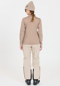 Beige langærmet top med tekstureret stof, kombineret med lyse beige bukser med sidelukninger og sorte detaljer ved manchetterne.