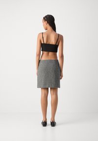 Top cropped noir et jupe mini en pied-de-poule gris. La jupe présente une coupe droite et une taille plate. Le modèle porte des chaussures noires.