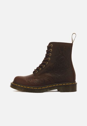 Botte en cuir marron foncé à lacets avec motifs floraux embossés, couture jaune sur la semelle et languette à l'arrière.