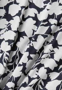 Tissu noir avec de grandes silhouettes florales blanches et des formes de feuilles créant un motif audacieux à fort contraste.