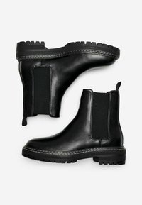 Botas Chelsea de cuero negro con paneles laterales elásticos, suela de goma resistente, tira en el talón y detalles de costura blanca en contraste.