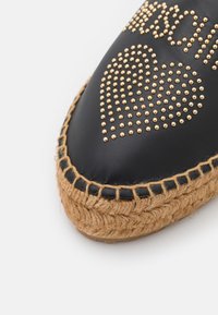 Black leather espadrille with gold studded heart design, woven jute sole, and decorative stitching along the edge.