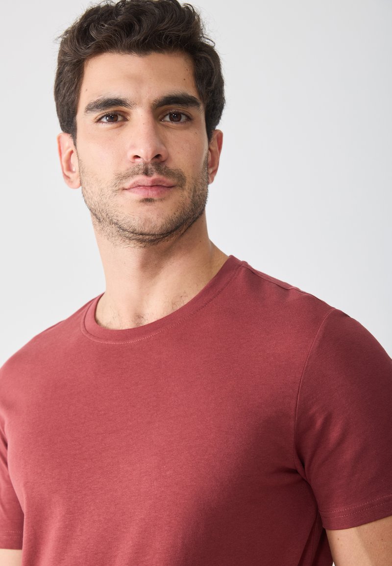 T-shirt en coton bordeaux avec un col rond, des manches courtes et une texture lisse. Design simple sans motifs ni accents visibles.