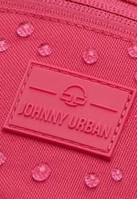 Růžový látkový batoh s texturovaným povrchem, embosovaným logem "JOHNNY URBAN" a malými, lesklými kruhovými akcenty.