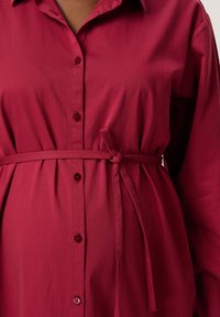Rote Hemdjacke mit Kragen, taillierter Bindegürtel und weichem, glattem Stoff. Mit passenden Knöpfen auf der Vorderseite.