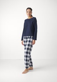 Marinblå långärmad tröja parat med rutig pyjamasbyxor i marinblått och vitt. Byxorna har resår i midjan och fållar.