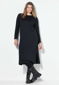 Pitkähihainen musta mekko, jossa on sivuaukko, valmistettu pehmeästä kankaasta. Yhdistetty mustiin nilkkureihin, joissa on paksu pohja. Tasainen pinta, minimalistinen muotoilu.