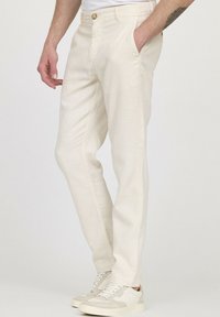 Pantalons en lin beige clair à coupe droite, avec des poches latérales et une fermeture à boutons. Associés à des baskets de couleur claire.