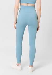 Vysoké legíny v světle modrém ribbovém materiálu, s bezšvým designem, doplněné o bílé tenisky.