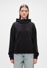 Μαύρο hoodie με φερμουάρ από μαλακό ύφασμα και μπροστινή τσέπη. Διαθέτει υπερμεγέθη γραμμή, μακριά μανίκια και ένα μικρό λογότυπο στο στήθος.