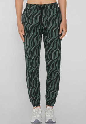 Jogging avec un motif vert et un design rayé noir de tigre, une taille élastique et des ourlets resserrés, associés à des chaussures de sport grises et blanches.