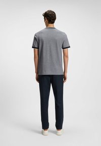 Gray short-sleeve t-shirt with navy collar detail, paired with navy pinstriped pants and white sneakers. Back view showing the fit.
