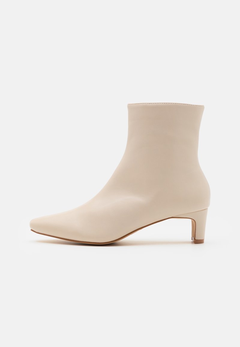Bottine beige en cuir avec bout pointu et petit talon kitten, design minimaliste sur fond blanc uni.