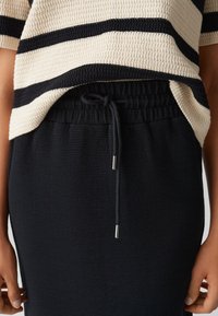 Schwarzer, strukturierter Rock mit einem Kordelzugbund und silbernen Akzenten, kombiniert mit einem gestreiften Oberteil in Creme und Marineblau.