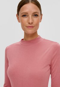 Haut à manches longues et col haut en tissu côtelé rose doux, avec une silhouette ajustée et une texture subtile.