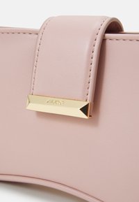 Jasnoróżowa torebka z eko skóry z prostokątnym złotym akcentem z wypukłym logo marki. Gładka faktura i minimalistyczny design.