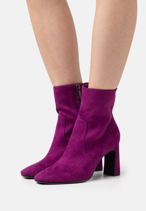 Stivaletti in suede viola con punta squadrata e tacco alto a blocco. Presentano una cerniera laterale e una texture liscia.