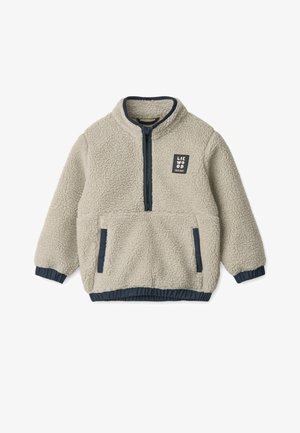 Šviesiai smėlio spalvos fliso striukė su užtrauktuku priekyje, tamsiai mėlynomis detalėmis ir elastinėmis rankovėmis. Ant krūtinės yra kvadratinis logotipo ženklelis.