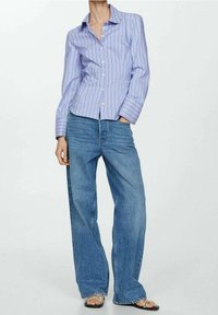 Chemise à rayures bleu clair et blanc avec boutons et manches longues, associée à un jean en denim bleu taille haute à jambes larges et des sandales noires.