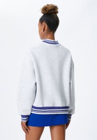 Szara bluza z prążkowanym kołnierzem w fioletowe i białe paski, w oversize'owym kroju i ze ściągaczami na rękawach; zestawiona z niebieską spódnicą.