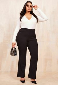 Biely bodysuit s dlhým rukávom a výstrihom do V, v kombinácii s čiernymi nohavicami s vysokým pásom. Modelka drží malú čiernu kabelku. Textúrované pozadie.
