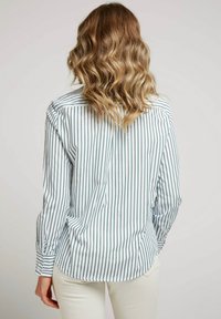 Chemise à rayures avec de fines rayures vertes sur fond blanc, manches longues et ourlet arrondi. Tissu lisse et léger.