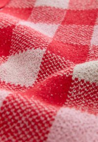 Czerwono-różowa tkana tkanina w kratkę z teksturowanym wzorem dzianiny; miękka, puszysta faktura z widocznymi detalami splotu i kontrastującymi blokami kolorów.