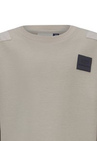 Felpa beige chiaro con scollo rotondo. Presenta pannelli sulle spalle testurizzati di una tonalità più chiara e una patch quadrata blu scuro.