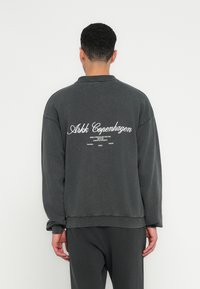 Czarnoszary, oversize'owy sweter z wysokim kołnierzem, z białym nadrukiem na plecach oraz ściągaczami przy rękawach i u dołu.