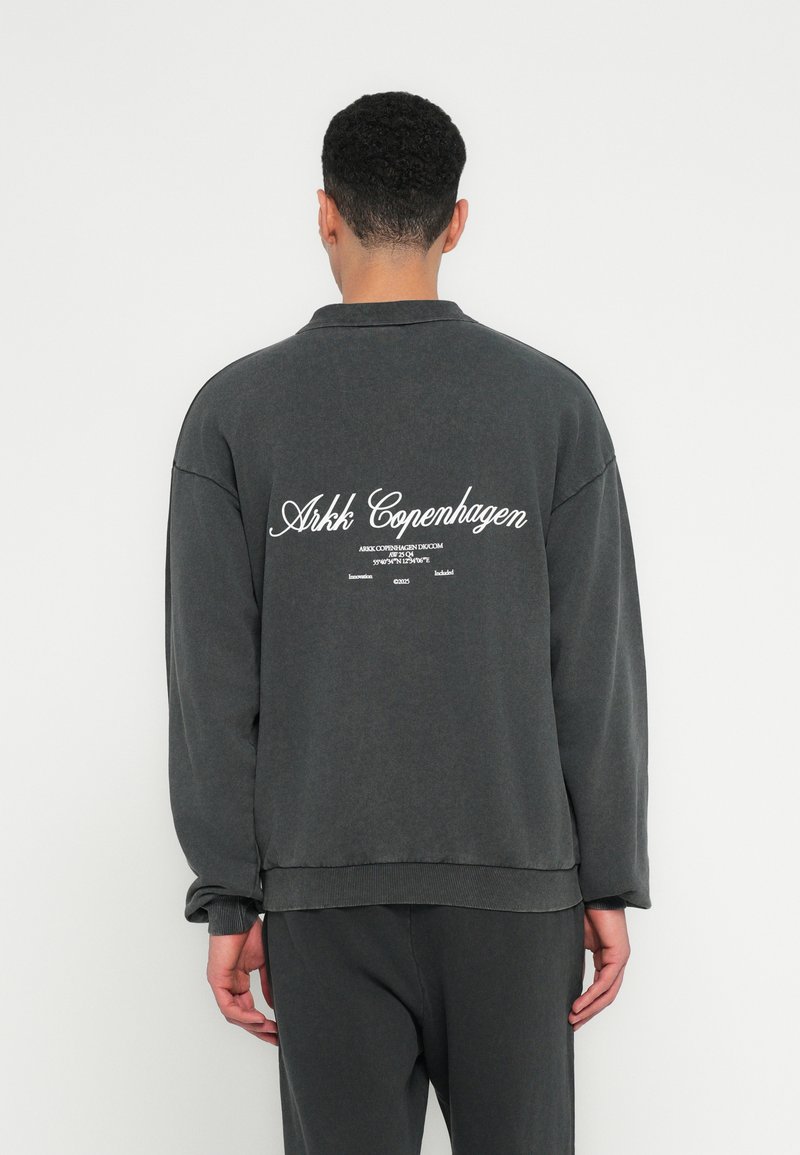 Dunkelgrauer oversized Sweatshirt mit hohem Kragen, auf der Rückseite mit weißem Schriftzug-Branding und gerippten Bündchen und Saum.