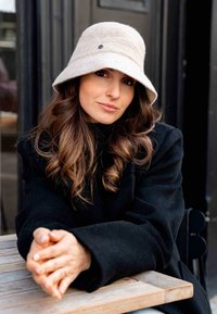 Beige wool bucket hat with a wide brim and a subtle textured band, paired with a black coat, resting on a wooden table.