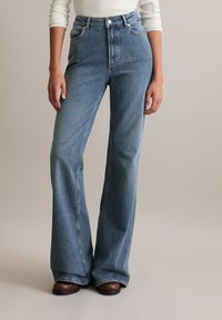 Hoge taille blauwe spijkerbroek met flared pijpen, twee voorzakken, subtiele vervaging en een rits met knoopsluiting.