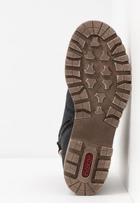 Calzado negro con suela de goma texturizada, que presenta un diseño de banda de rodadura estampada y un cierre con cremallera en el lateral para un fácil acceso.