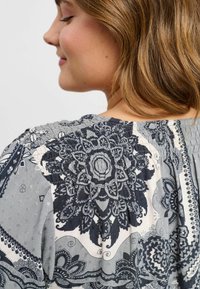 Grå bluse med mønster, der har indviklede mandala-designs, struktureret smocking langs halsudskæringen og blødt, let stof.