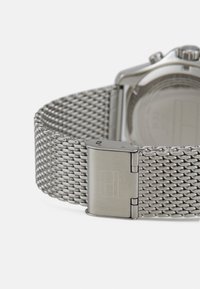 Silberne Maschenarmbanduhr mit einem polierten Stahlverschluss. Verfügt über eine glatte Textur und eine rechteckige Markierung am Verschluss. Runder Ziffernblatt.
