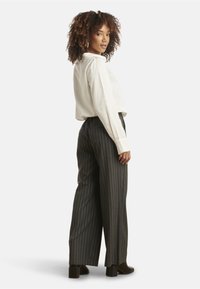 White long-sleeve shirt, paired with high-waisted dark gray pinstriped trousers and brown heeled ankle boots. Model facing right.