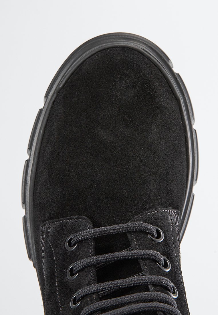 Botín de suede negro con puntera redondeada, suela de goma gruesa y ojetes metálicos para los cordones. La superficie texturizada y los acentos cosidos realzan el diseño.
