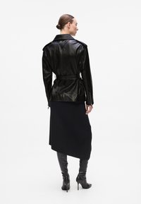 Black leather jacket with a belted waist, shoulder epaulettes, and zippers. Worn over a fitted black skirt and knee-high black stiletto boots.