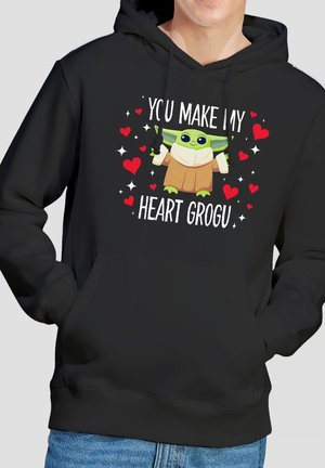 Black hoodie with cartoon Grogu holding a cup, surrounded by red hearts and white sparkles, text reads "You make my heart Grogu."