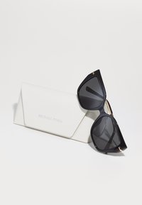 Ochelari de soare negri, unghiulari, cu lentile întunecate și accente aurii, asortați cu un etui din piele ecologică albă, embossat cu "Michael Kors."