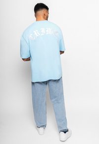 Lys blå oversized t-skjorte med "CRIME" trykt i hvitt på ryggen, kombinert med lys blå denim bukser og hvite sneakers.
