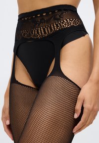 Meias de rede pretas com um alto design de cós rendado. O cós apresenta padrões intrincados e recortes, contrastando com o tecido liso das pernas.