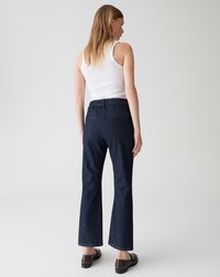 Jean flare bleu foncé avec une taille ajustée et une texture denim lisse, associés à un débardeur blanc et des chaussures sombres.