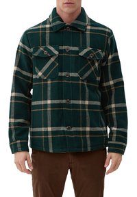 Giacca in flanella a quadri verdi con chiusura a bottoni, due tasche sul petto e una texture morbida. I dettagli includono linee beige e verde scuro.