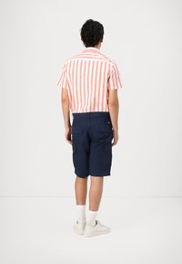 Camicetta a maniche corte, a righe rosa e bianche con colletto, abbinata a pantaloni cargo blu navy, calze bianche e scarpe chiare, vista da dietro.