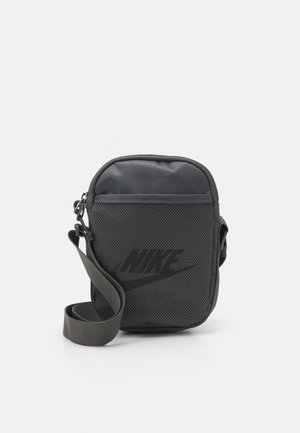 Petit sac à bandoulière noir Nike avec poche avant en mesh et sangle réglable, présenté sur un fond blanc uni.